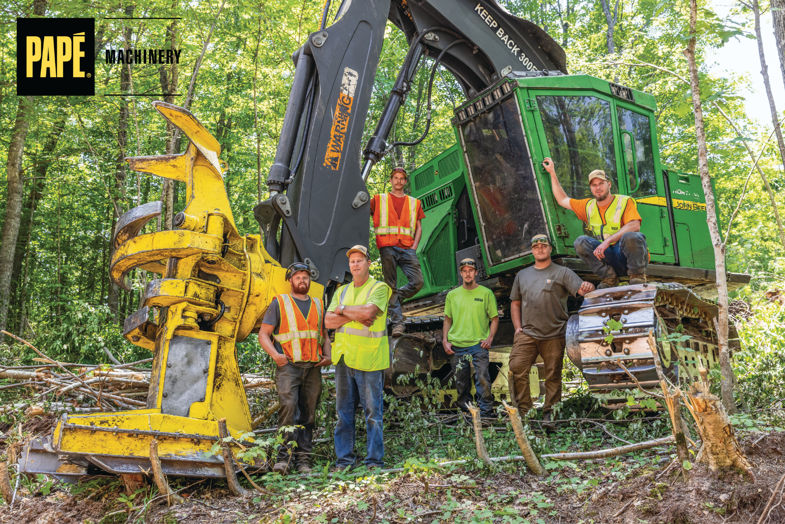 Logging crew standing beside a John Deere tracked forestry machine equipped with a harvesting attachment at a forest jobsite.